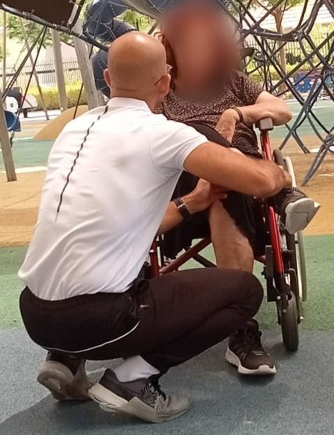 עידן בוזו כורע מול מתאמנת שיושבת בכיסא גלגלים ומדבר איתה בגובה העיניים