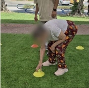 מתאמנת מבוגרת מתכופפת ומרימה קונוס מהדשא, בתרגול של התכופפות ושיווי משקל